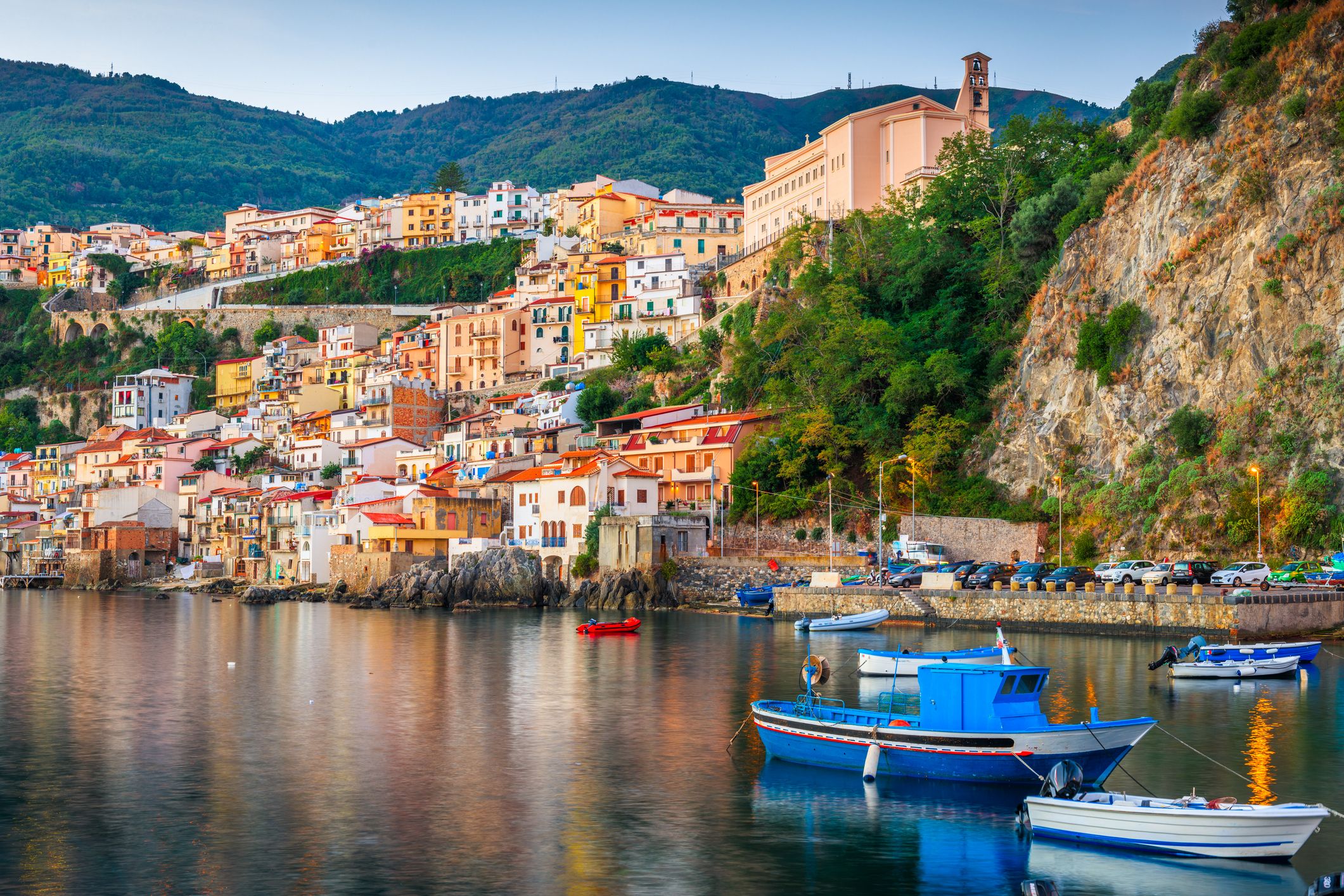 View across the water to a colourful town that spills down the side of a lush cliff