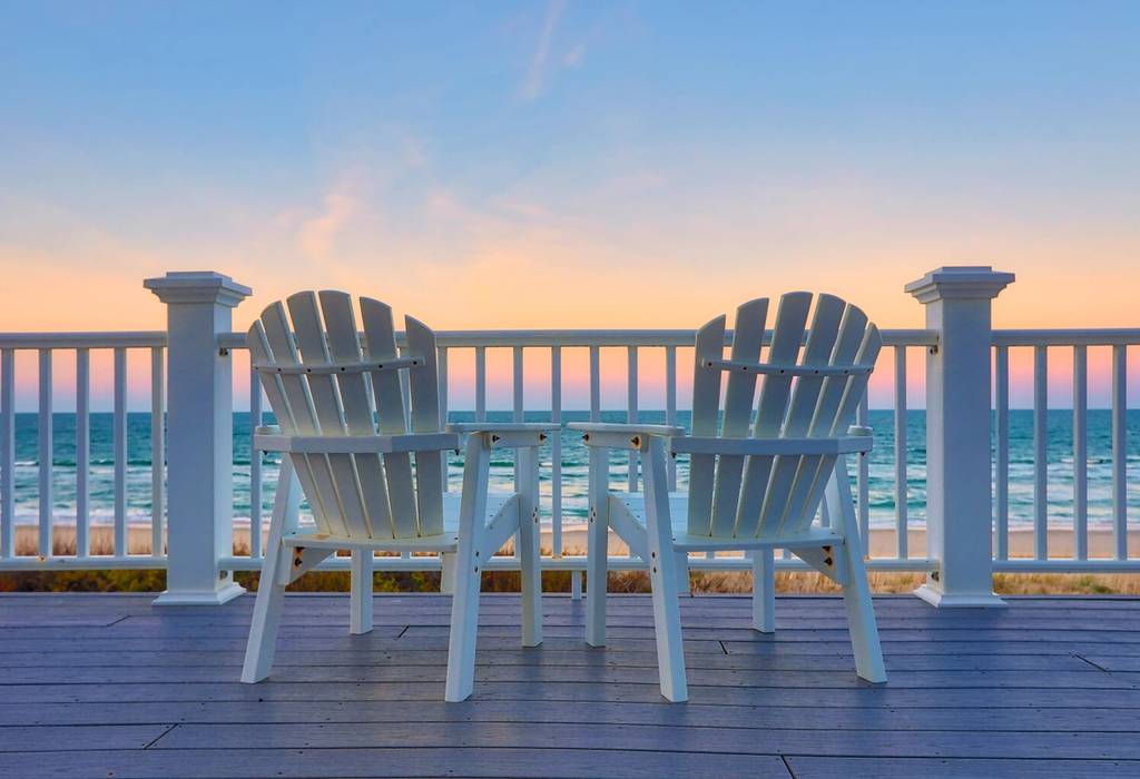 A view of the ocean showing two white deck chairs in front of the sea and sunset