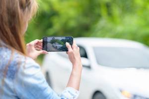 A smartphone in focus as a woman photographs a car accident, which is blurred in the background