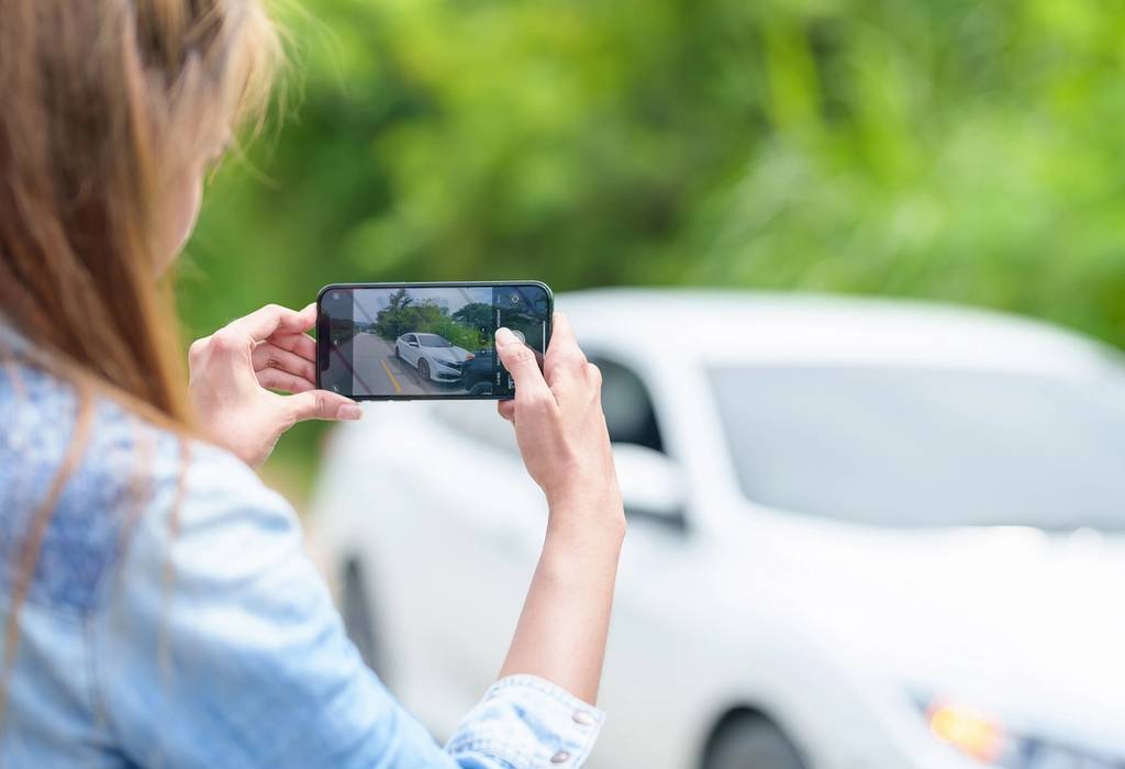 A smartphone in focus as a woman photographs a car accident, which is blurred in the background