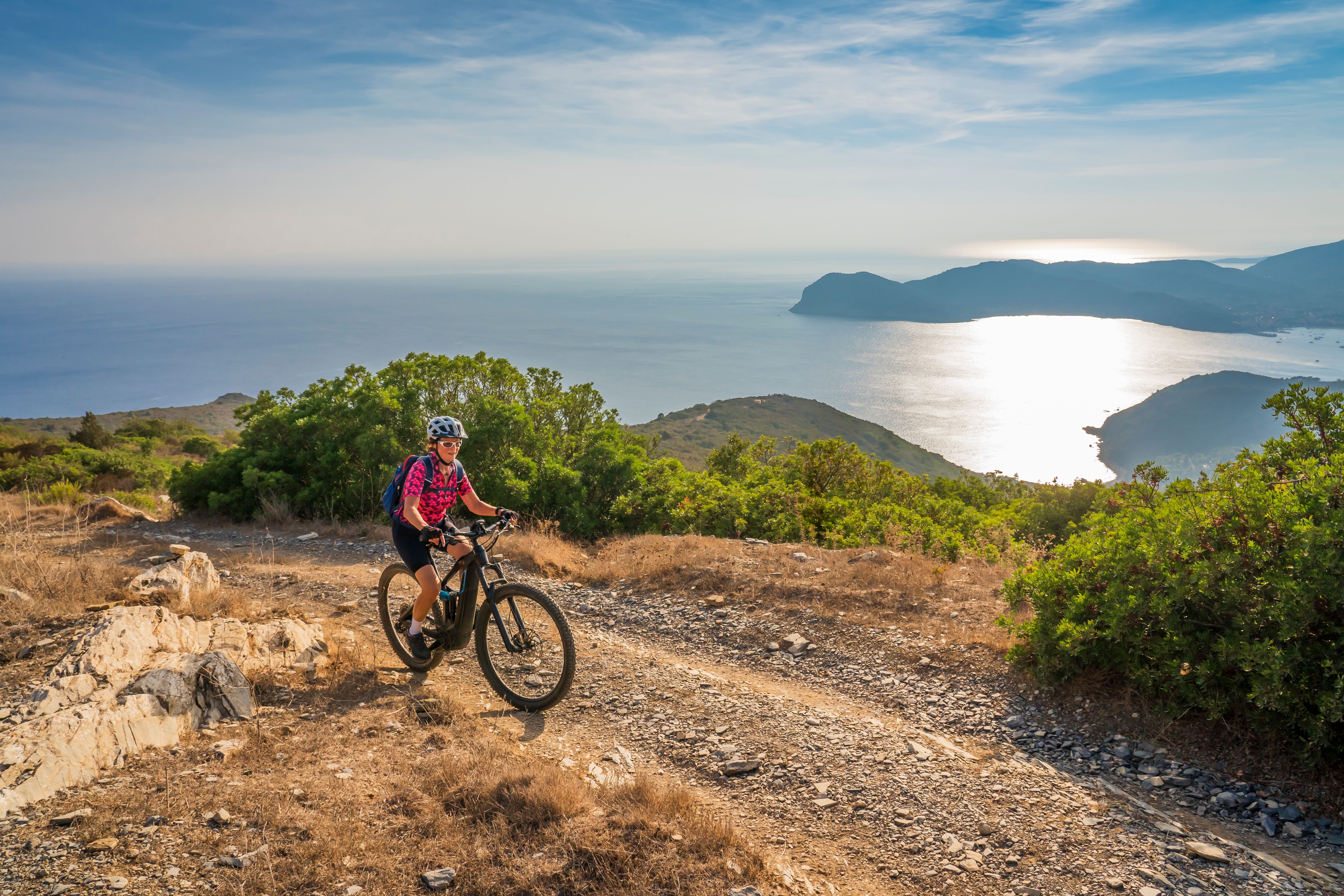 A woman mountain biking on a coastal trail above the mediterranean sea in Tuscany, Italy
