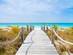A boardwalk leading between grasses and across sand to a white-sand beach with bright blue waters in the Caribbean