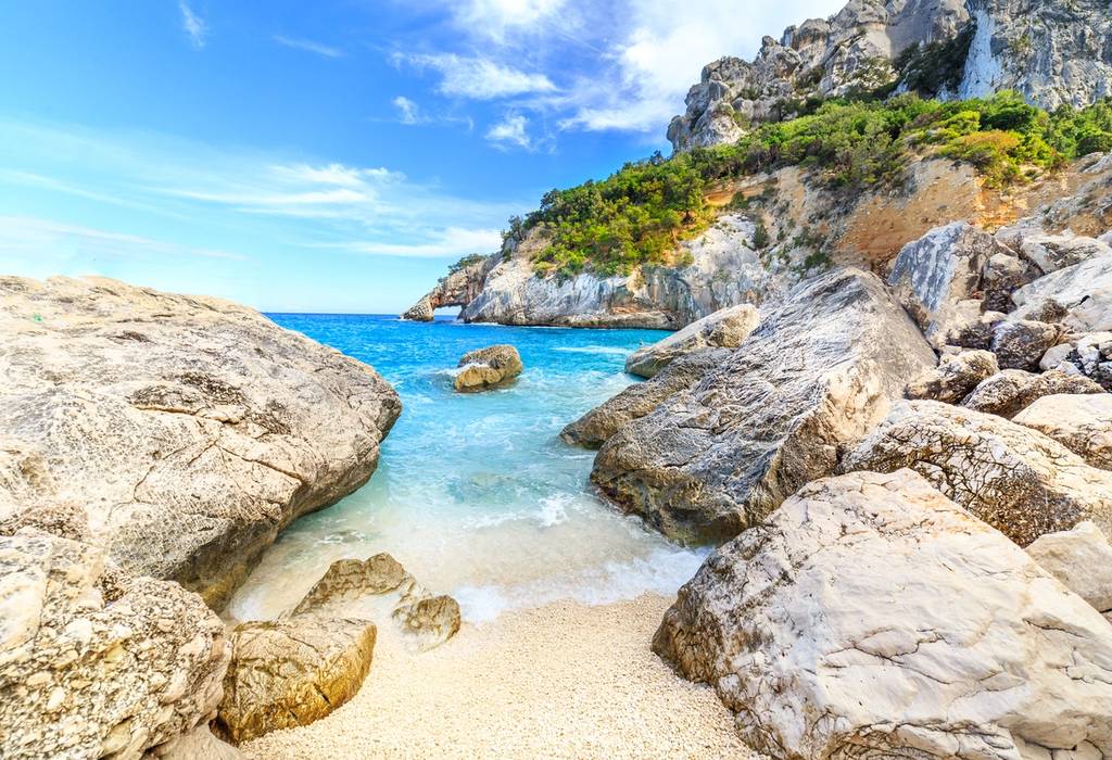 A view of water rushing on to the sand between the dramatic rocks at Cala Goloritze beach