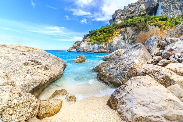 A view of water rushing on to the sand between the dramatic rocks at Cala Goloritze beach