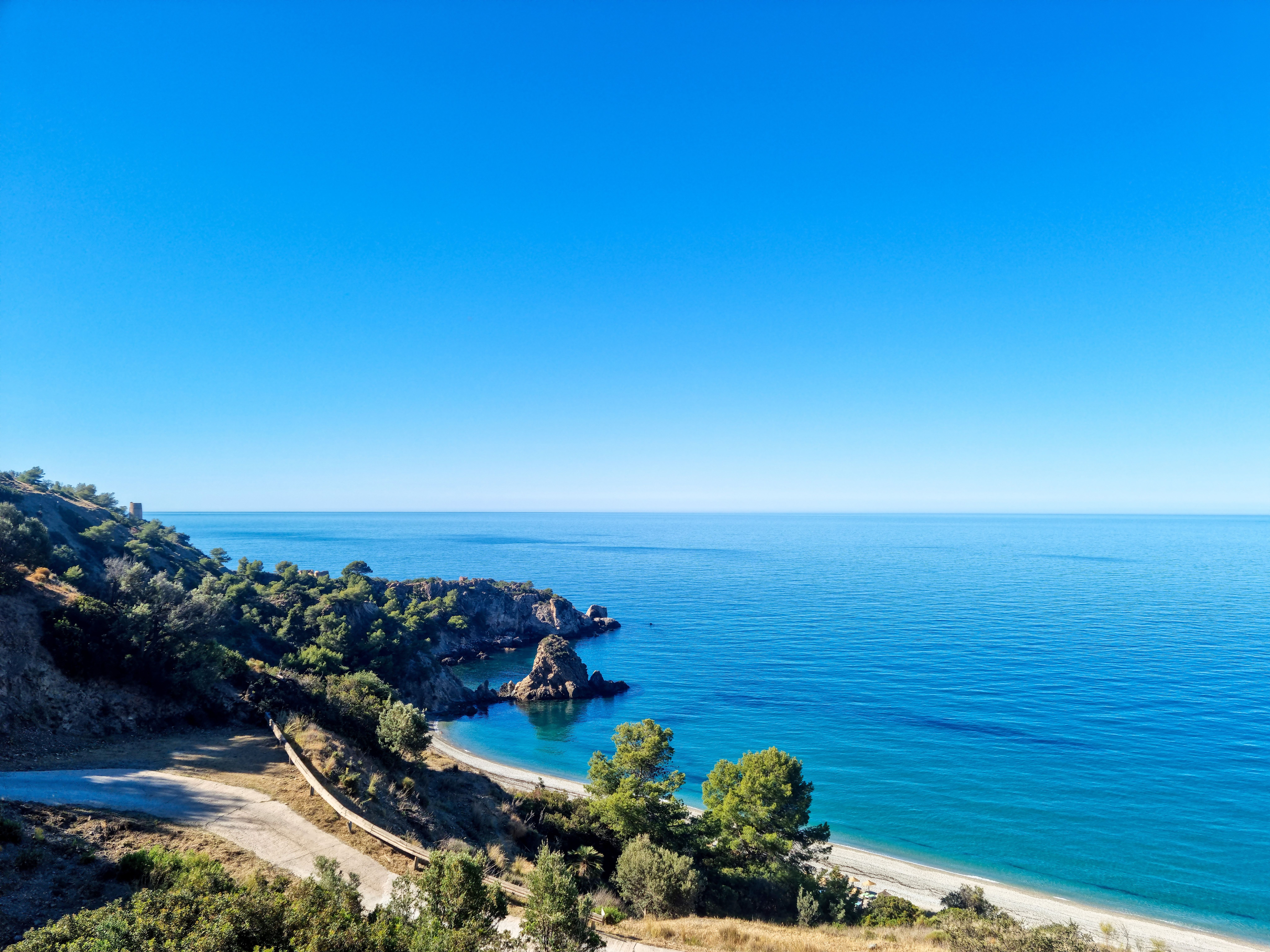 High angle view of an empty, gravelly beach with small rock formation jutting out of the azure water at one end.