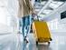 View of a woman walking with a bright yellow suitcase at an airport