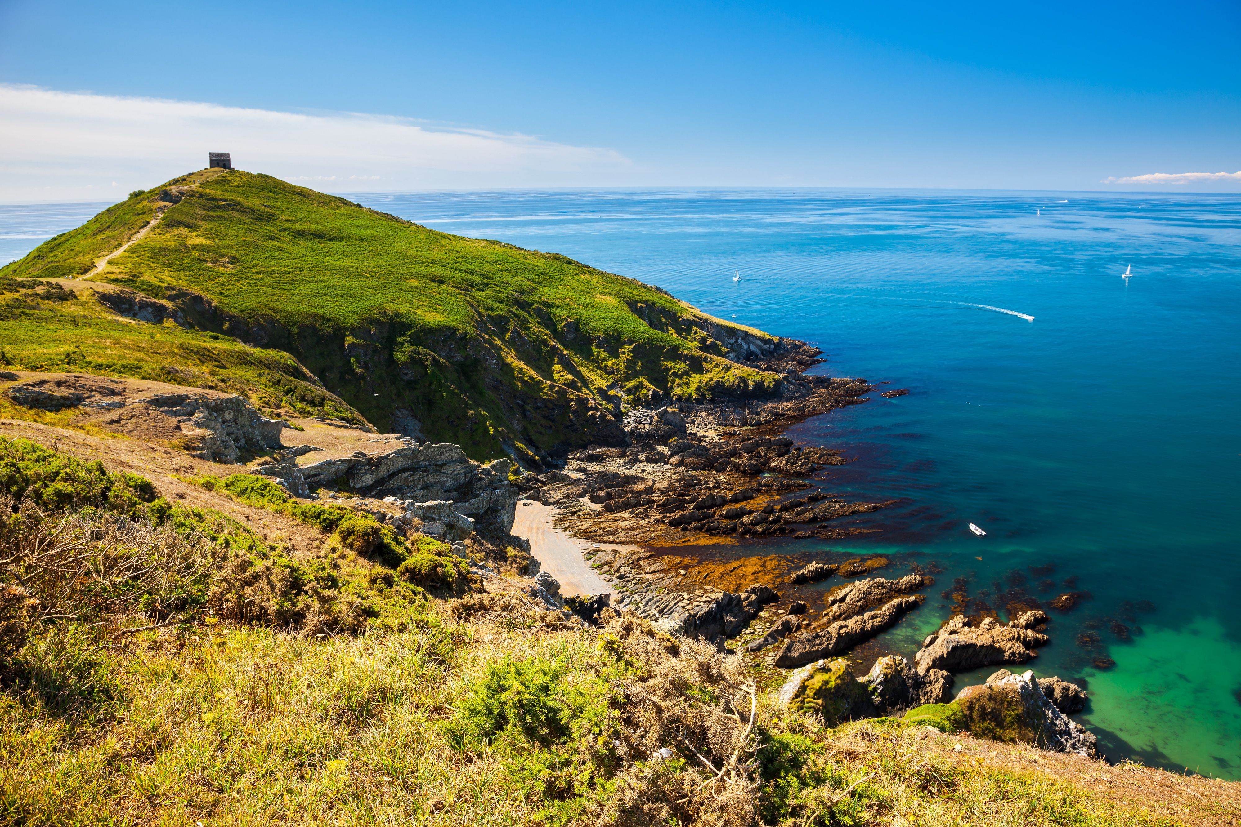 View of a grassy, rocky headland with a bench that overlooks the sparkling sea.