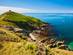 View of a grassy, rocky headland with a bench that overlooks the sparkling sea.