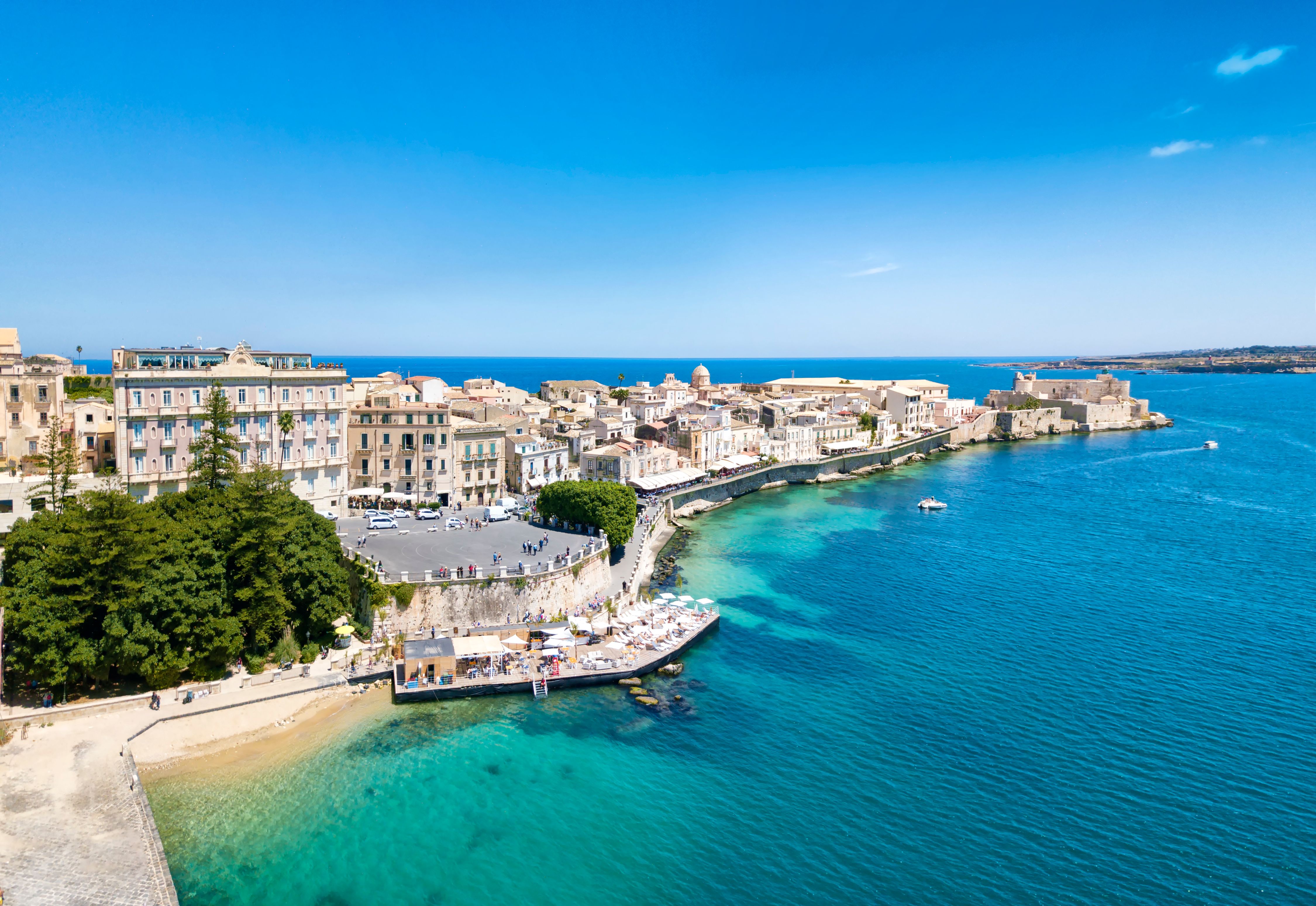 A coastal view of the island of Ortigia in Syracuse, Sicily with white-washed buildings and bright blue sea on a summer's day