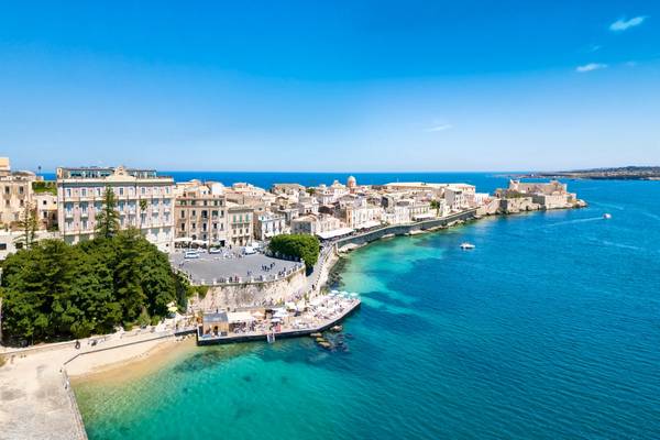 A coastal view of the island of Ortigia in Syracuse, Sicily with white-washed buildings and bright blue sea on a summer's day