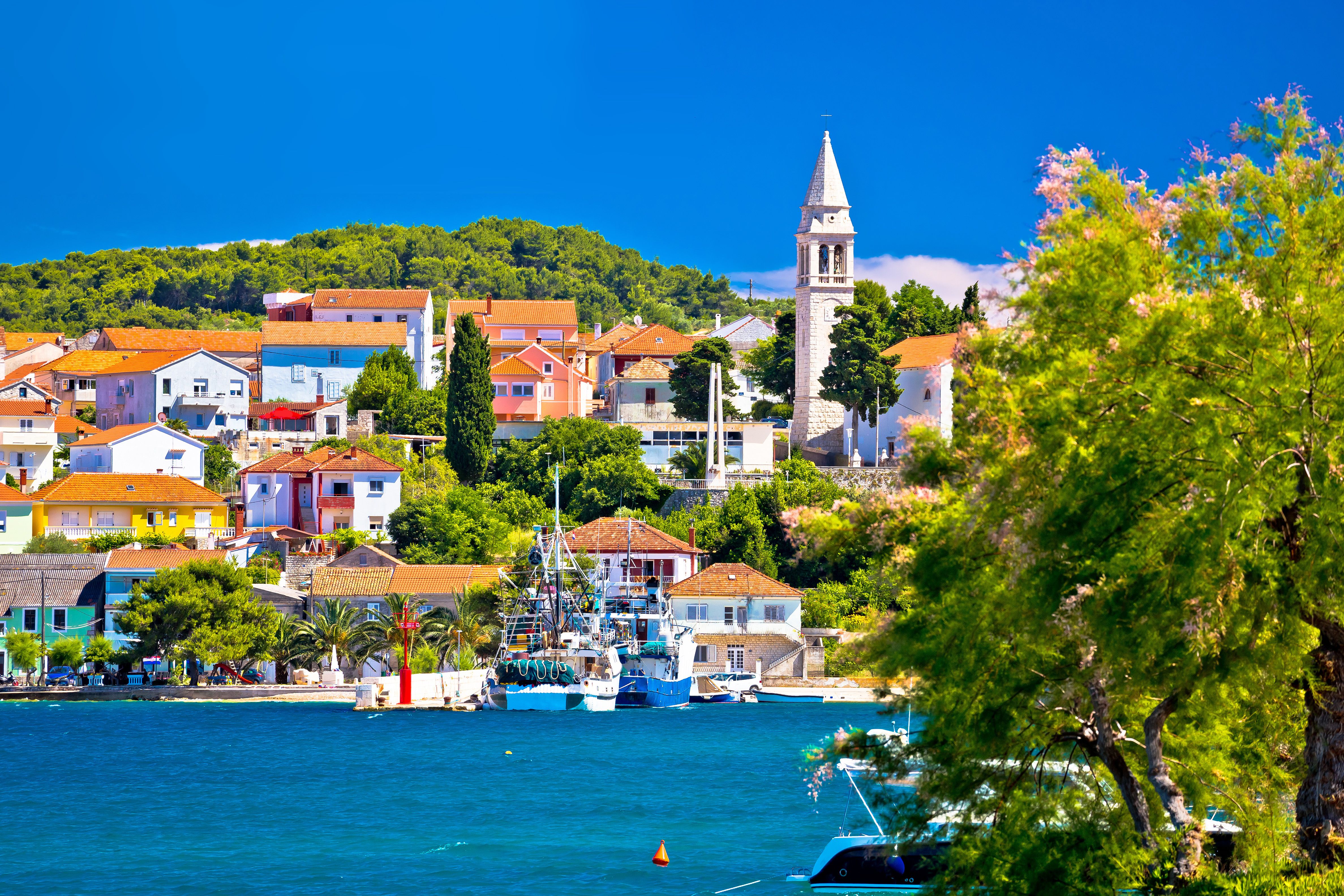 View of a coastal town with whitewashed, red-roofed houses and a tall church tower with a small harbourfront