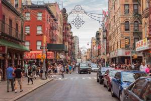 A view of a busy street in Chinatown, New York with brightly coloured shop fronts and lots of people walking along the pavements