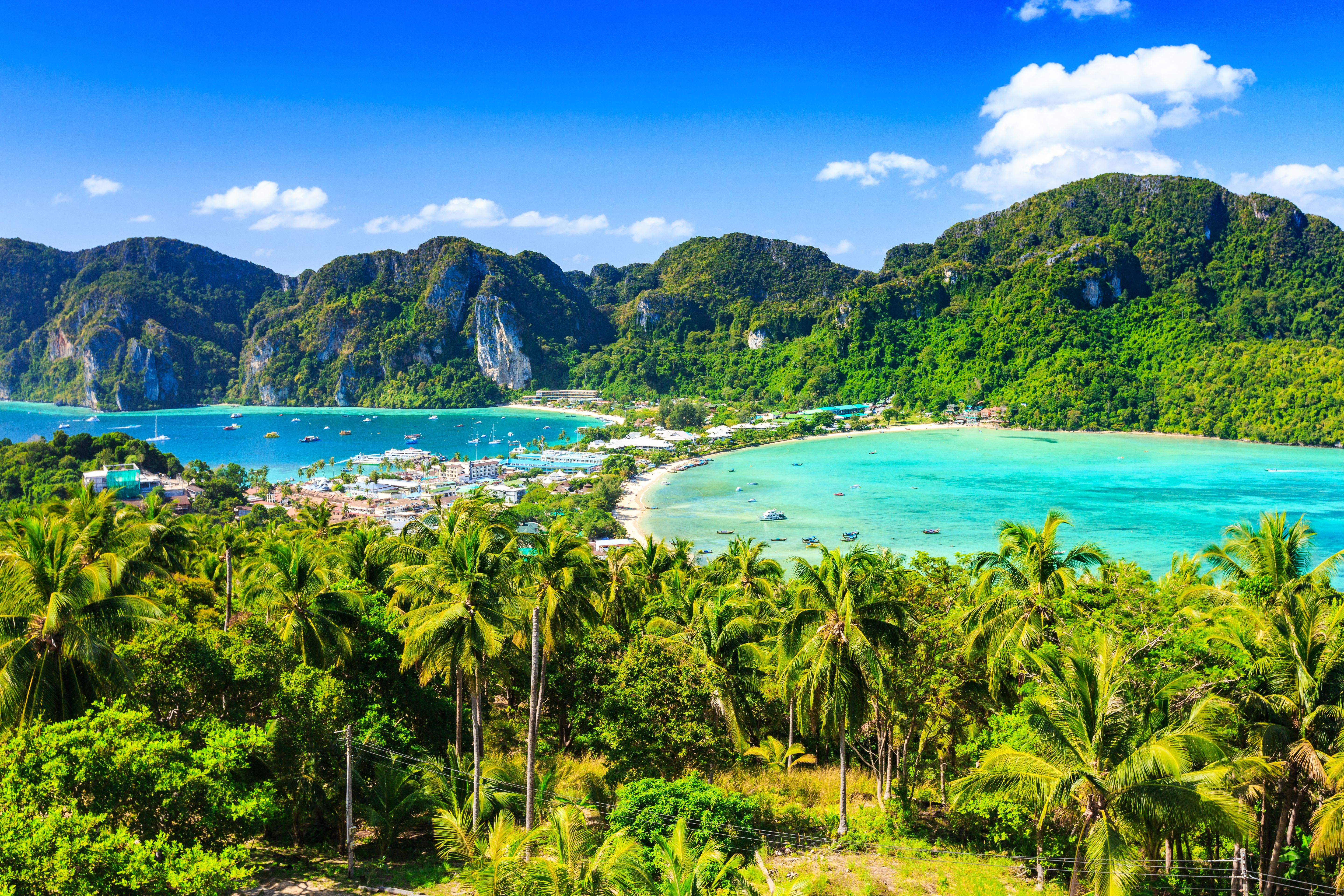 Aerial view of twin beaches separated by a tree-lined sandbar with lush mountains in the background