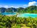 Aerial view of twin beaches separated by a tree-lined sandbar with lush mountains in the background
