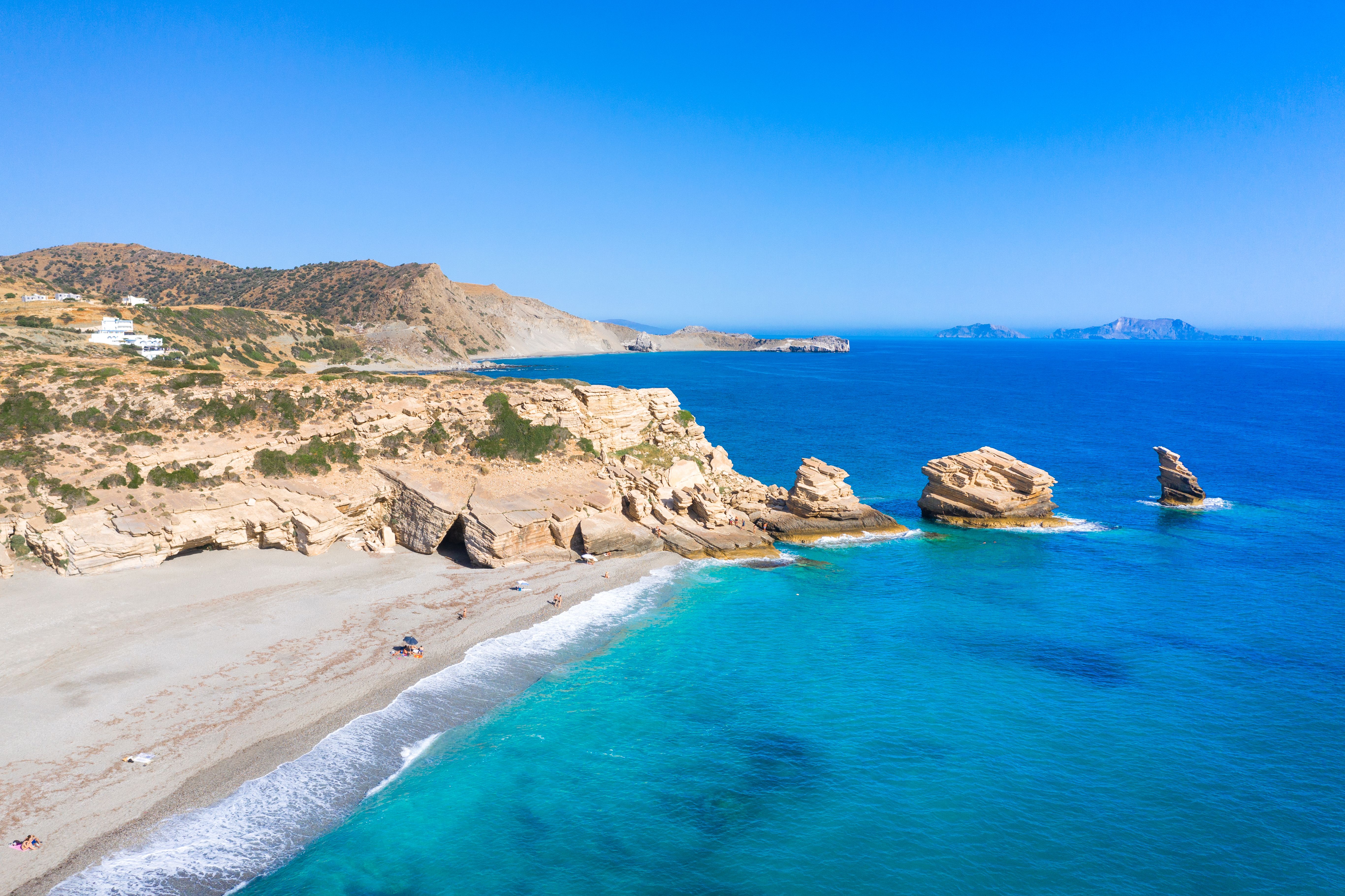 Drone view of a sandy beach with three rock formations jutting out of the turquoise sea.