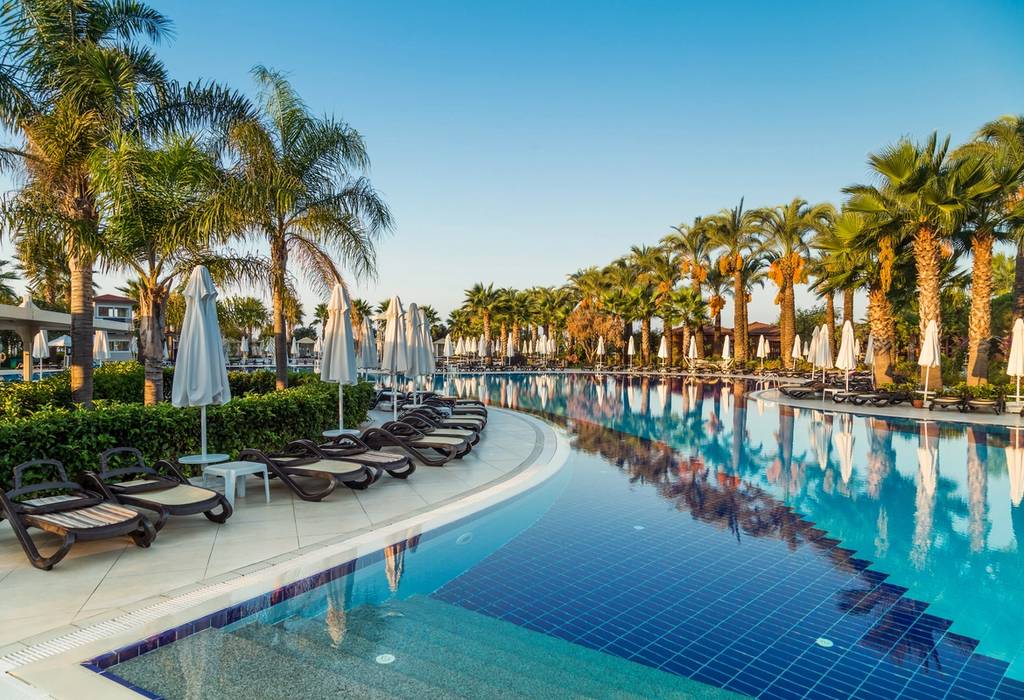 View of a hotel pool with sun beds, parasols and and palm trees at a resort in Antalya