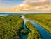 Aerial view of lush green wetlands during a soft, partly-cloudy sunset.