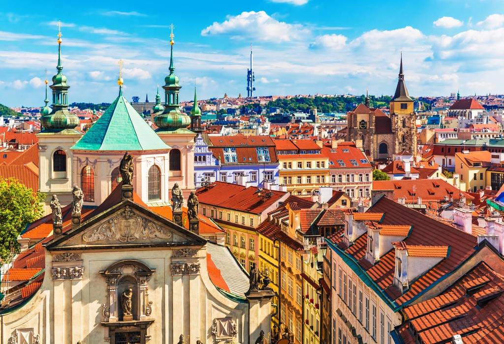 An aerial city view of Prague's terracotta rooftops and colourful buildings on a summer's day
