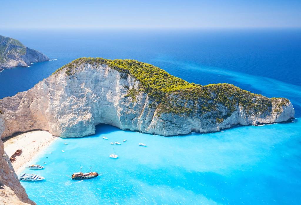 An aerial view on the famous Shipwreck Beach in Zante with boats on sparkling blue water and surrounded by white cliffs covered in green trees
