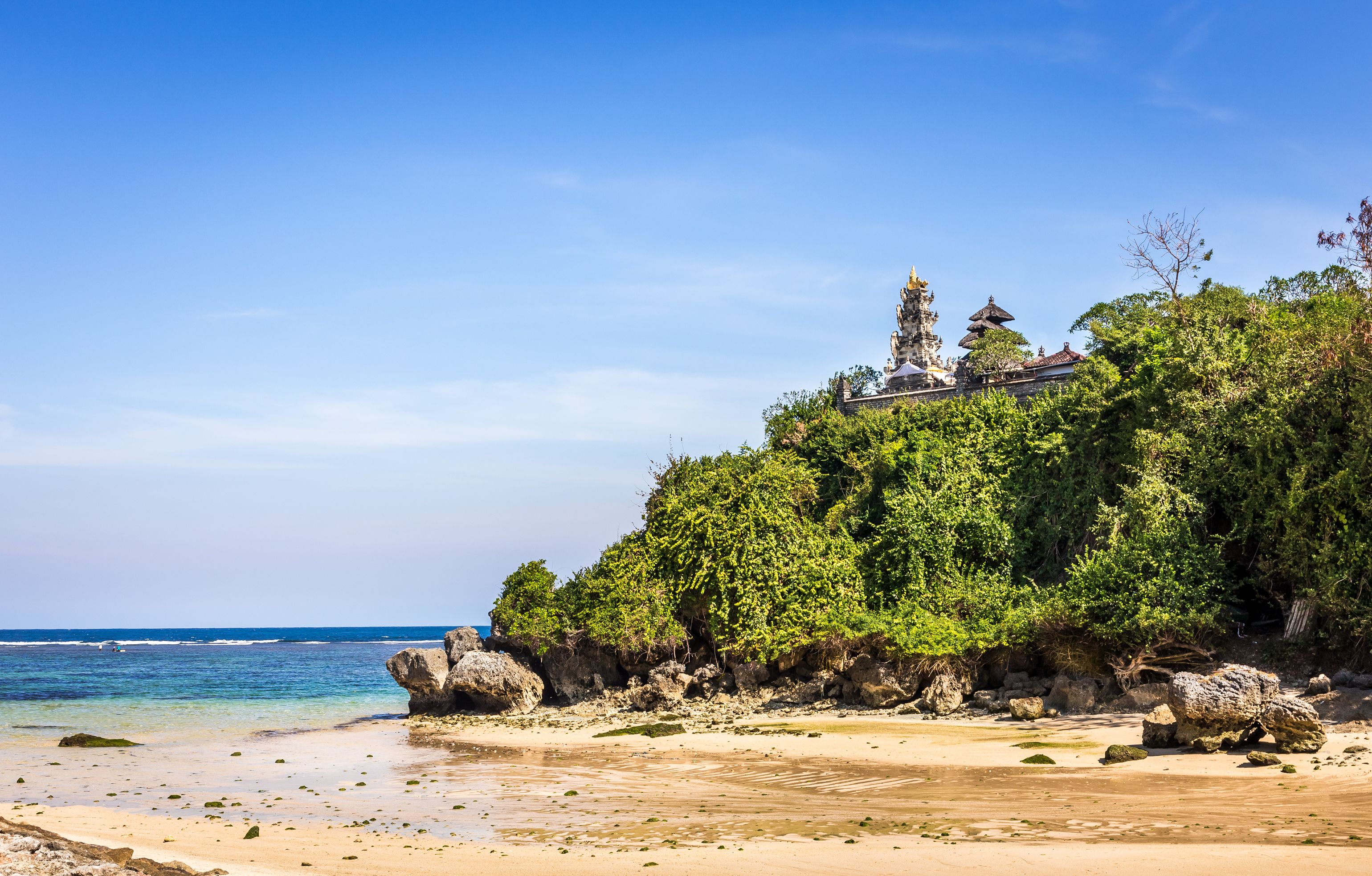 View of a golden, sandy beach with a traditional temple on a cliff overlooking the bay