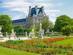 A view of the Tuileries Garden in Paris with lush green grass, bright flower beds and statue figures lining a path