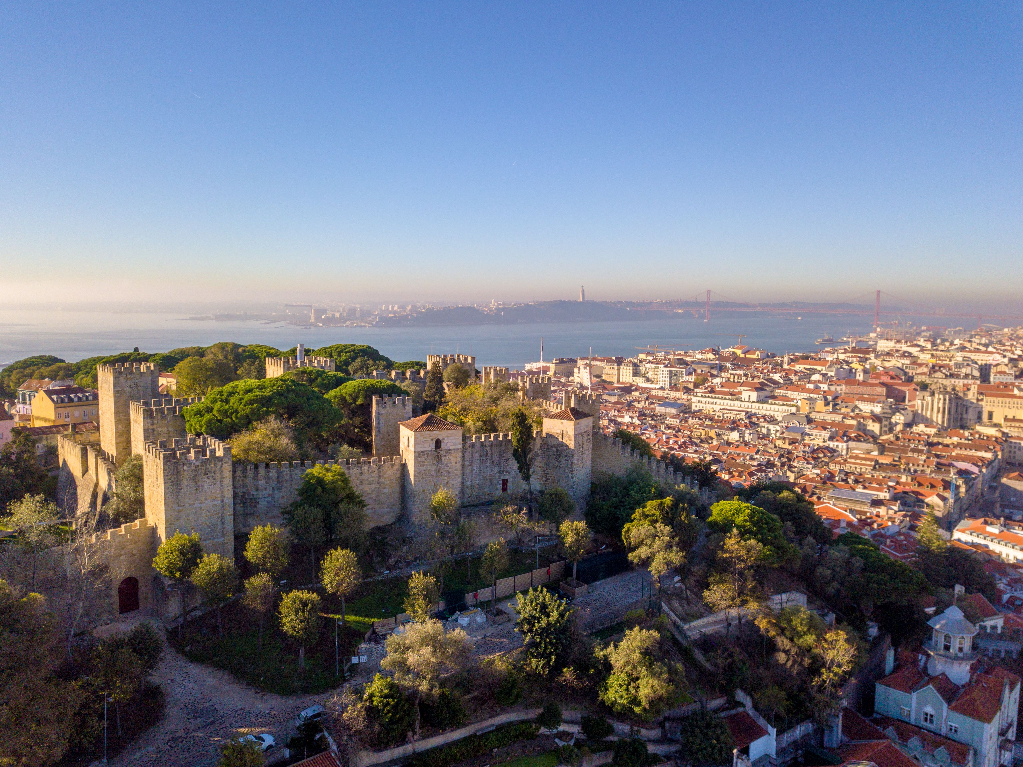 Aerial view of the turrets and walls of the São Jorge Castle atop a tree-covered hill in Lisbon