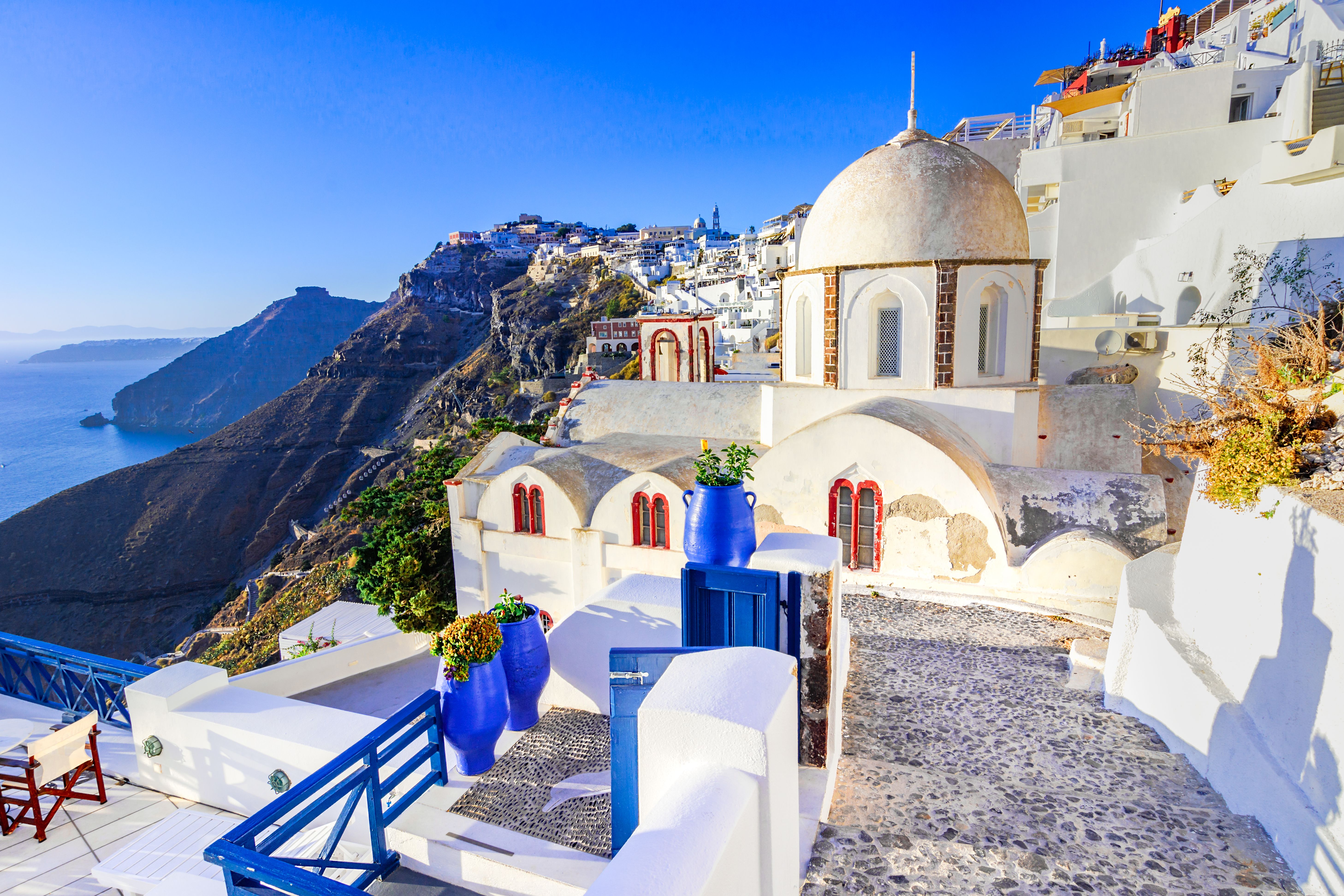 View of a white-domed building with the town of Fira clinging to the cliff behind it