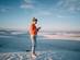 A woman in a bright orange jacket standing alone on endless white sand dunes using her phone