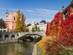 View of a bridge over a river and red baroque church flanked by autumnal foliage in Ljubljana