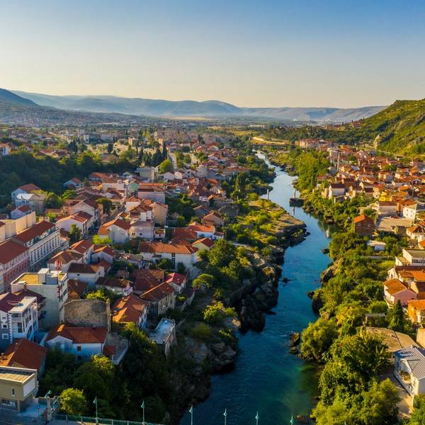 An aerial view over the old town and river in Mostar, Bosnia and Herzegovina with houses, river and mountains in the horizon on a sunny clear day