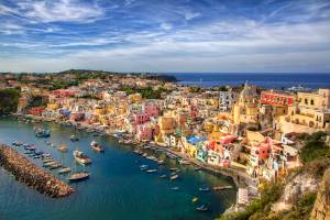 Aerial view on the colourful port town of Corricella on the island of Procida, with yellow and red-hued buildings overlooking a port filled with fishing boats