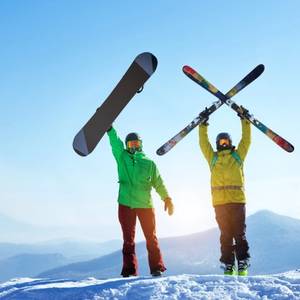 Skier and snowboarder stands at the top of a mountain with ski and snowboard in hands at the Sheregesh ski resort in Russia on a sunny winter day