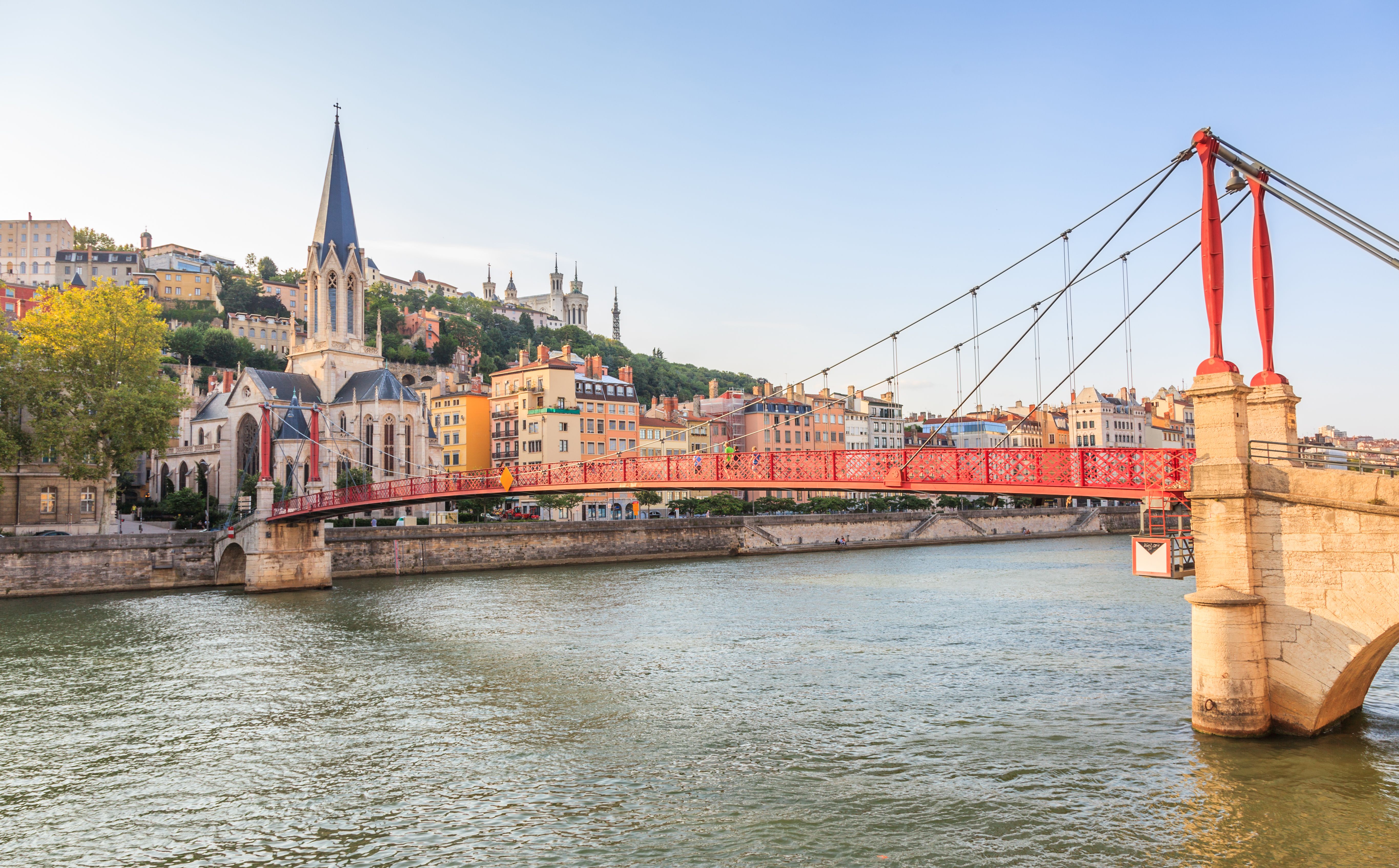 View of a red bridge spanning a river and looking towards a church and a row of pastel houses on the left bank