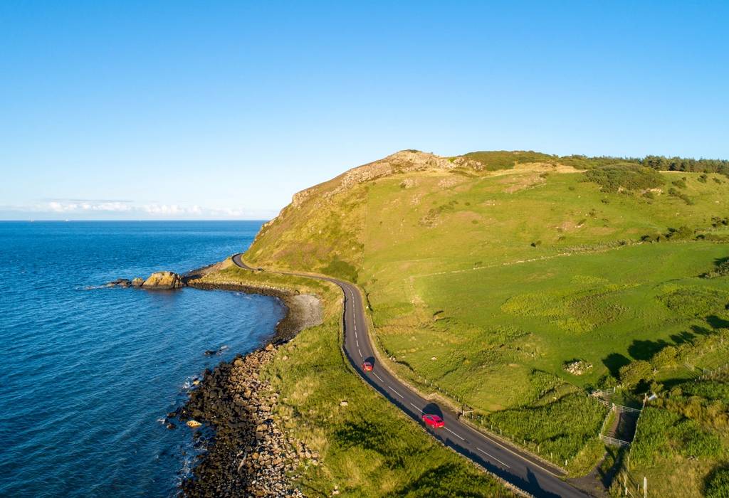 Aerial view of two red cars on the Causeway Coast Route, a scenic two-land road that hugs the coast in Northern Ireland