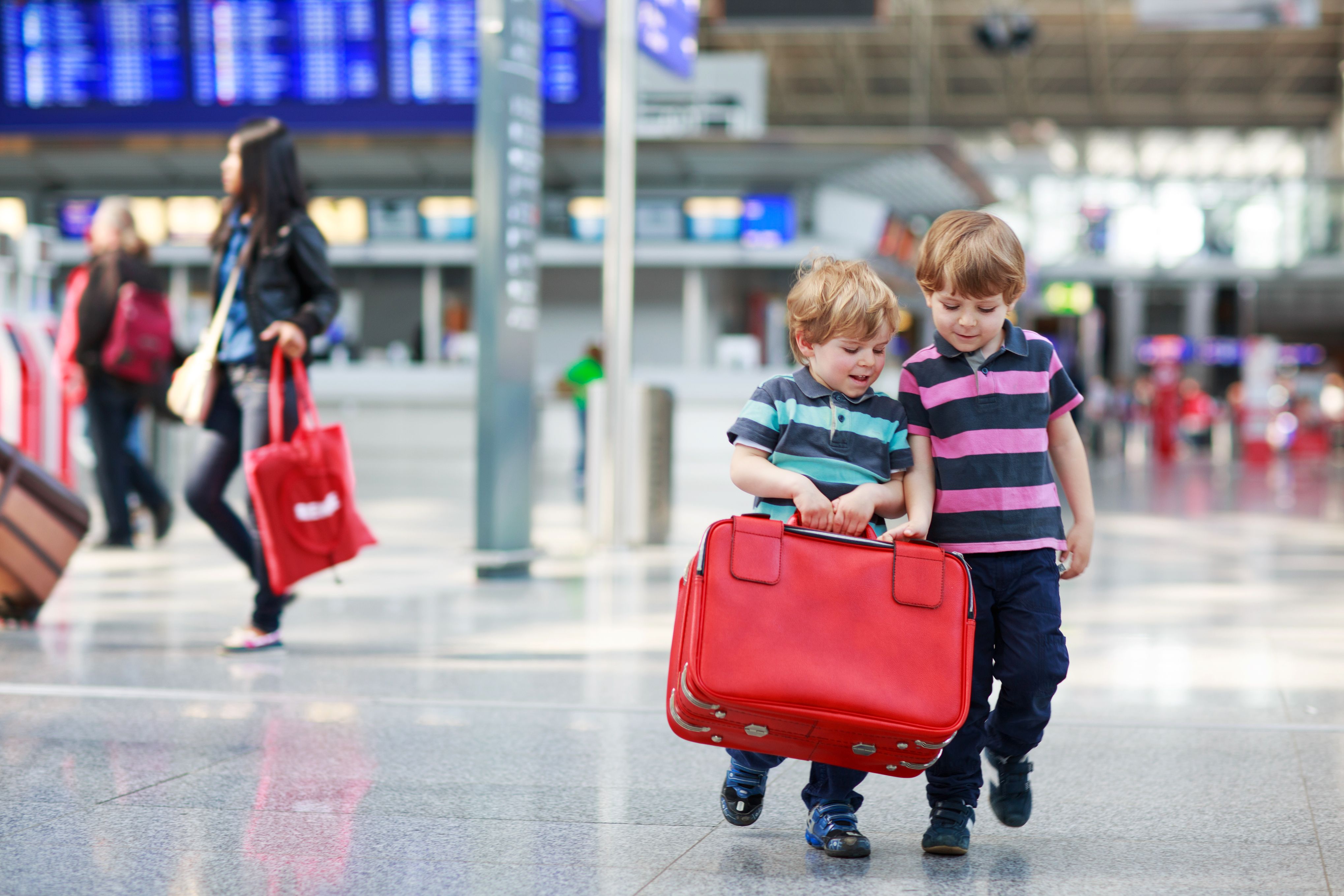 Two young boys carrying a red suitcase at an airport