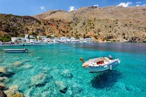 Small motorboats in clear water in the bay of Loutro town on Crete, Greece with mountains in the background