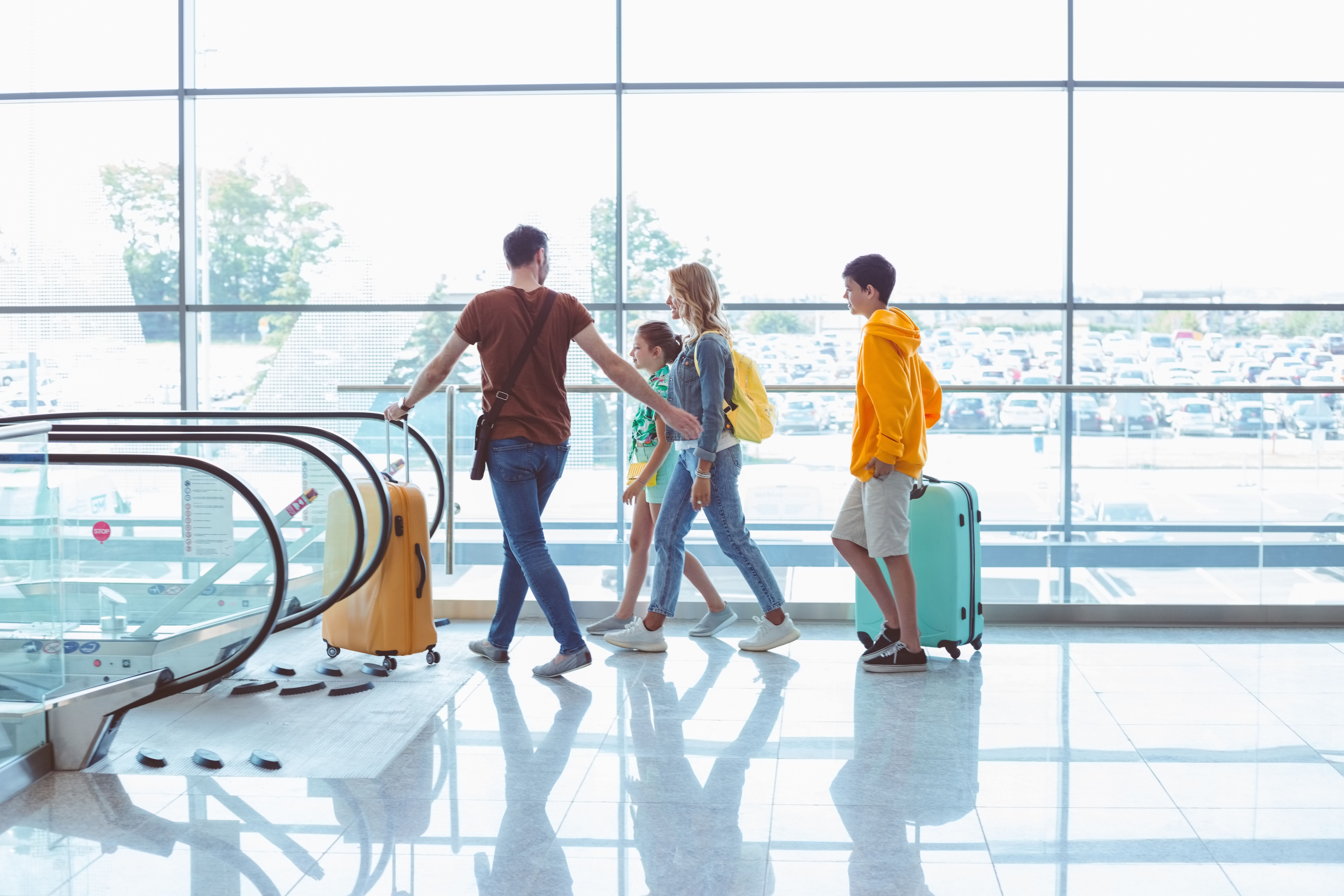 Side view of family with luggage walking at airport terminal, using escalator
