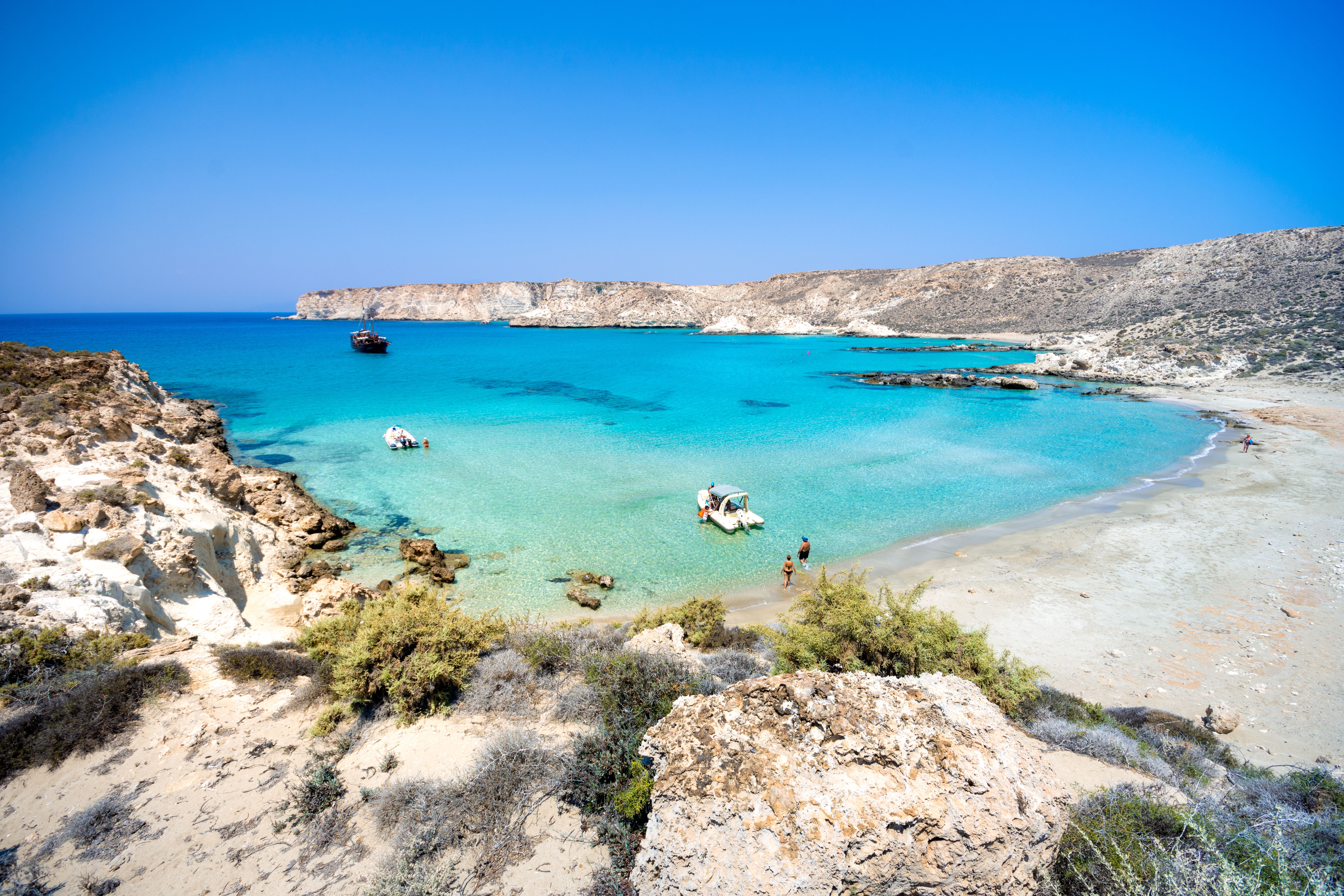 View of a curved white-sand beach with small boats bobbing in the clear turquoise waters.
