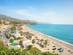 A view of Nerja beach and coastline in Costa del Sol, Spain with beach resorts and palm trees lining the coast and mountains in the background