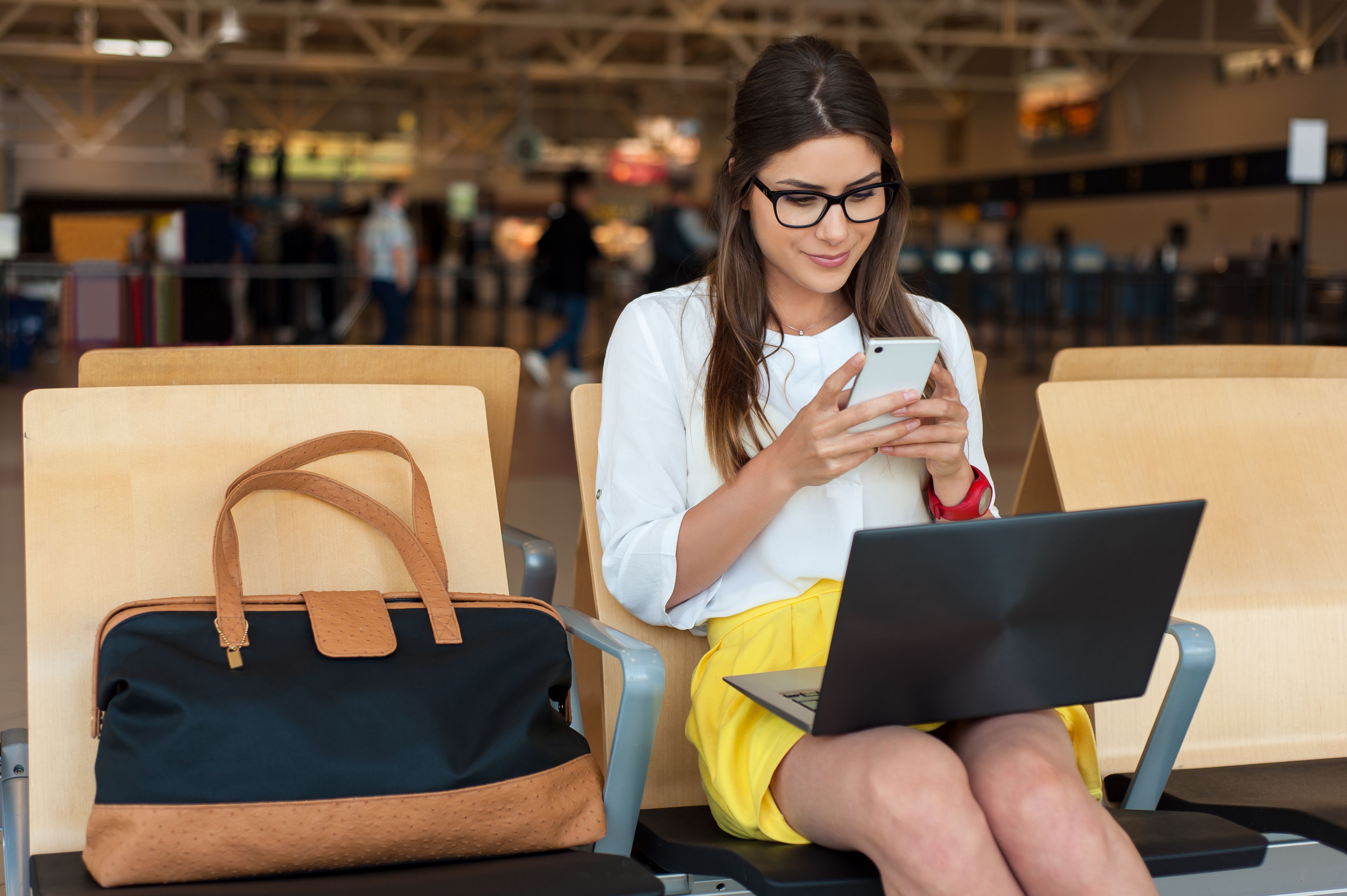 A woman on her phone and laptop in an airport departure lounge