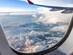 A view of the clouds and sky through the window of an aircraft also showing the plane wing