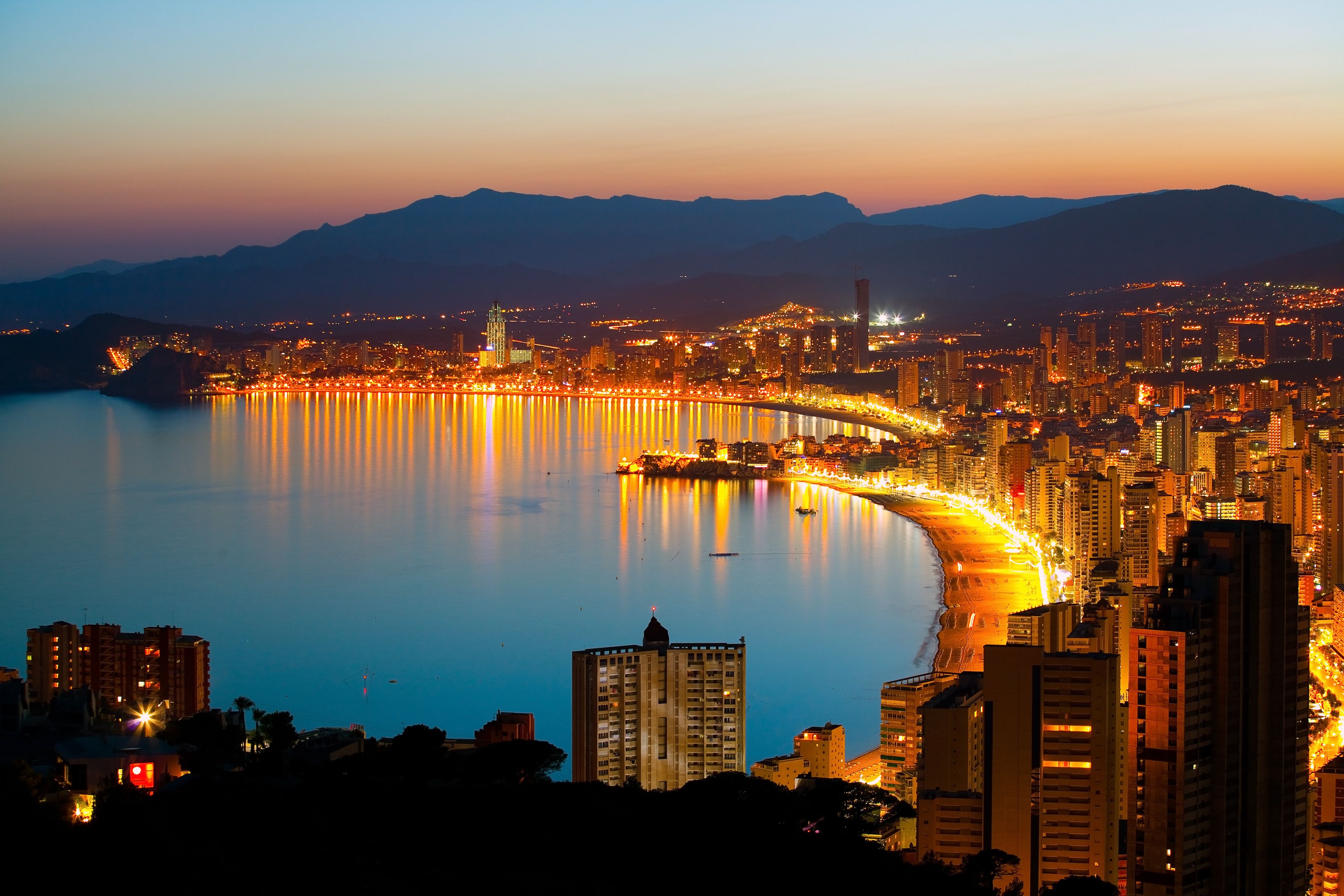 Panoramic aerial view of Benidorm city and beach aglow with lights as the sun sets