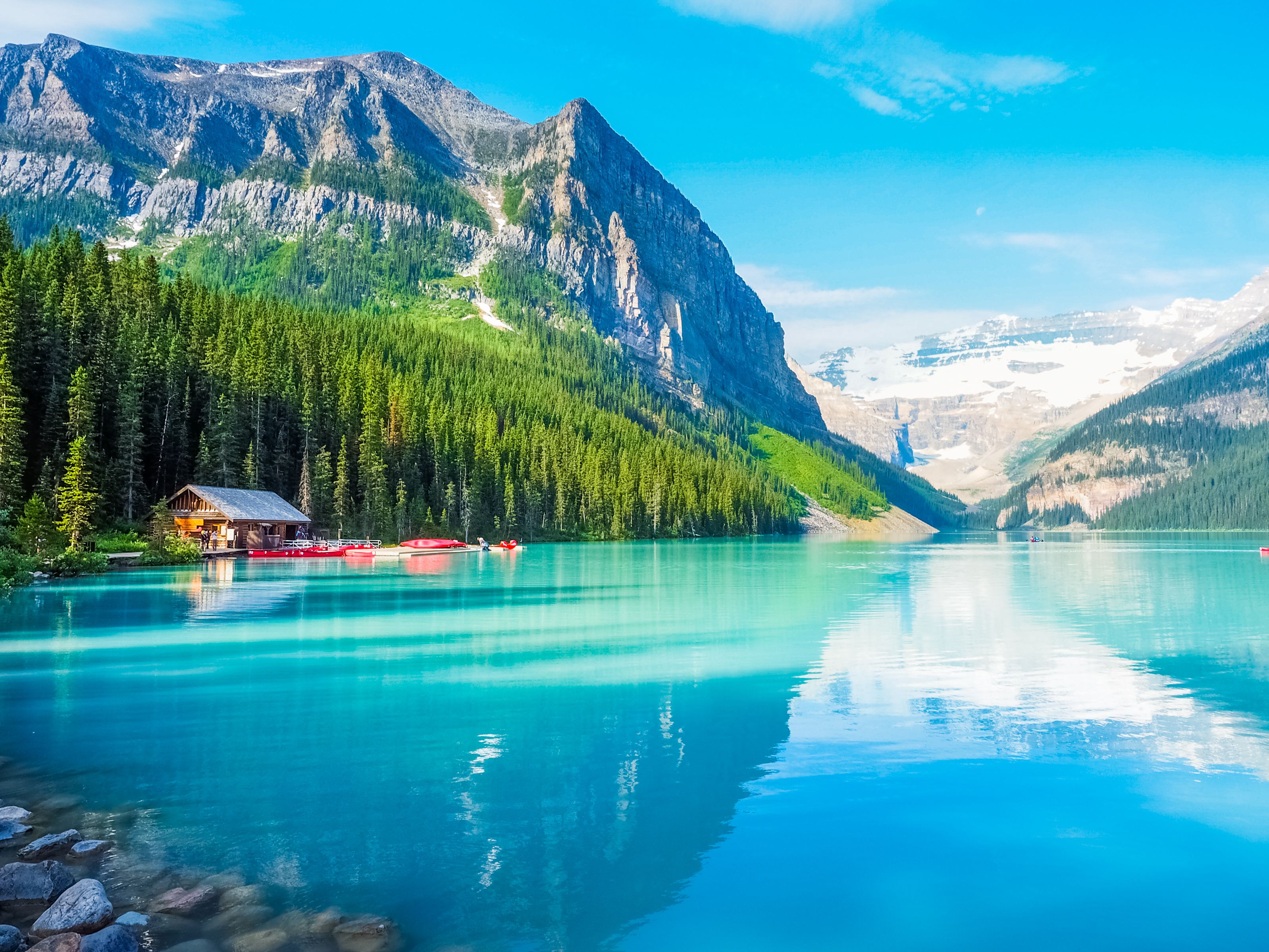 View of snow-capped mountains and small wooden cabin reflected in the brilliant blue waters of a lake in Canada