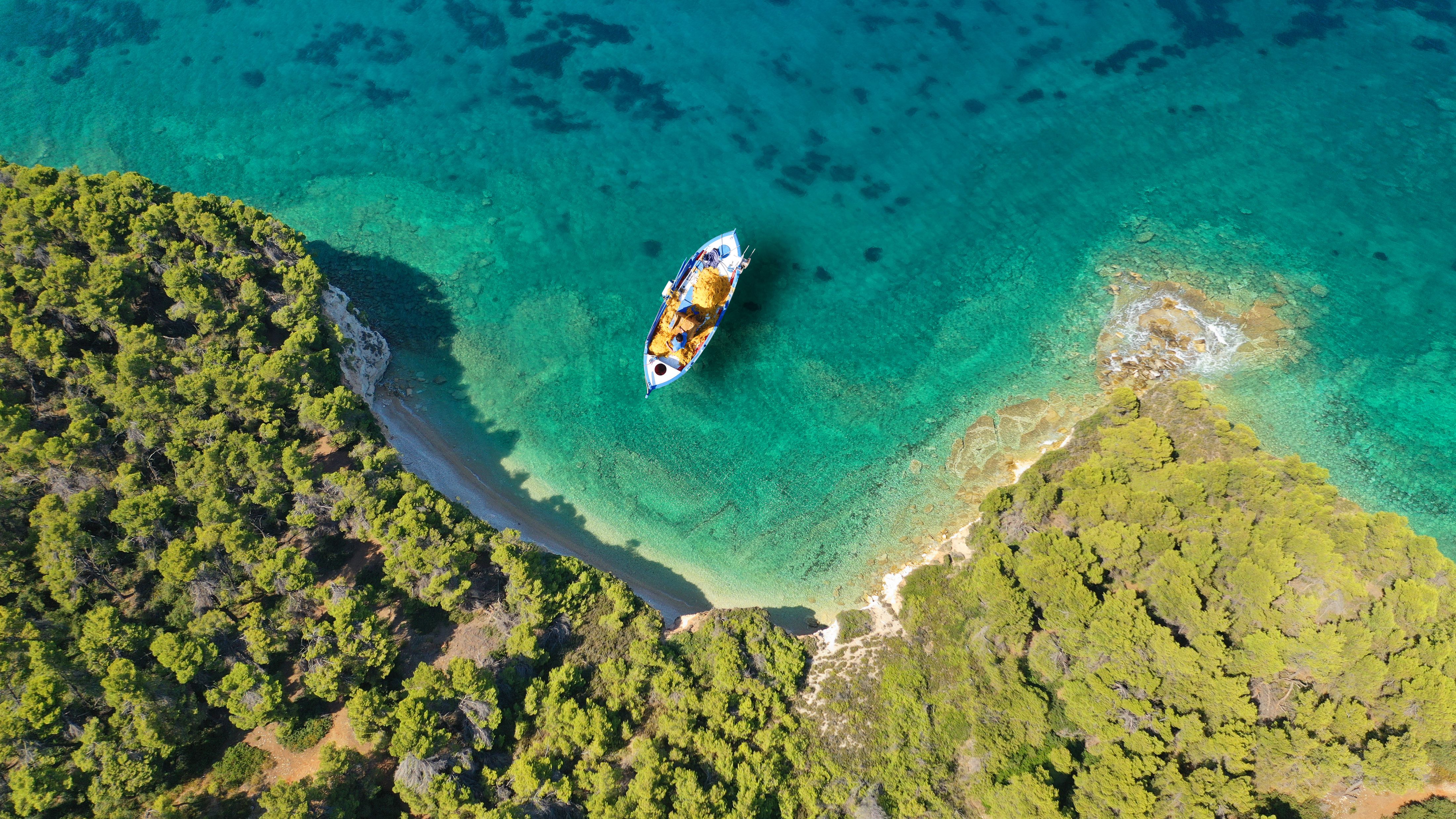 Aerial drone top down photo of traditional fishing boat anchored in a turquoise bay covered with pine trees.