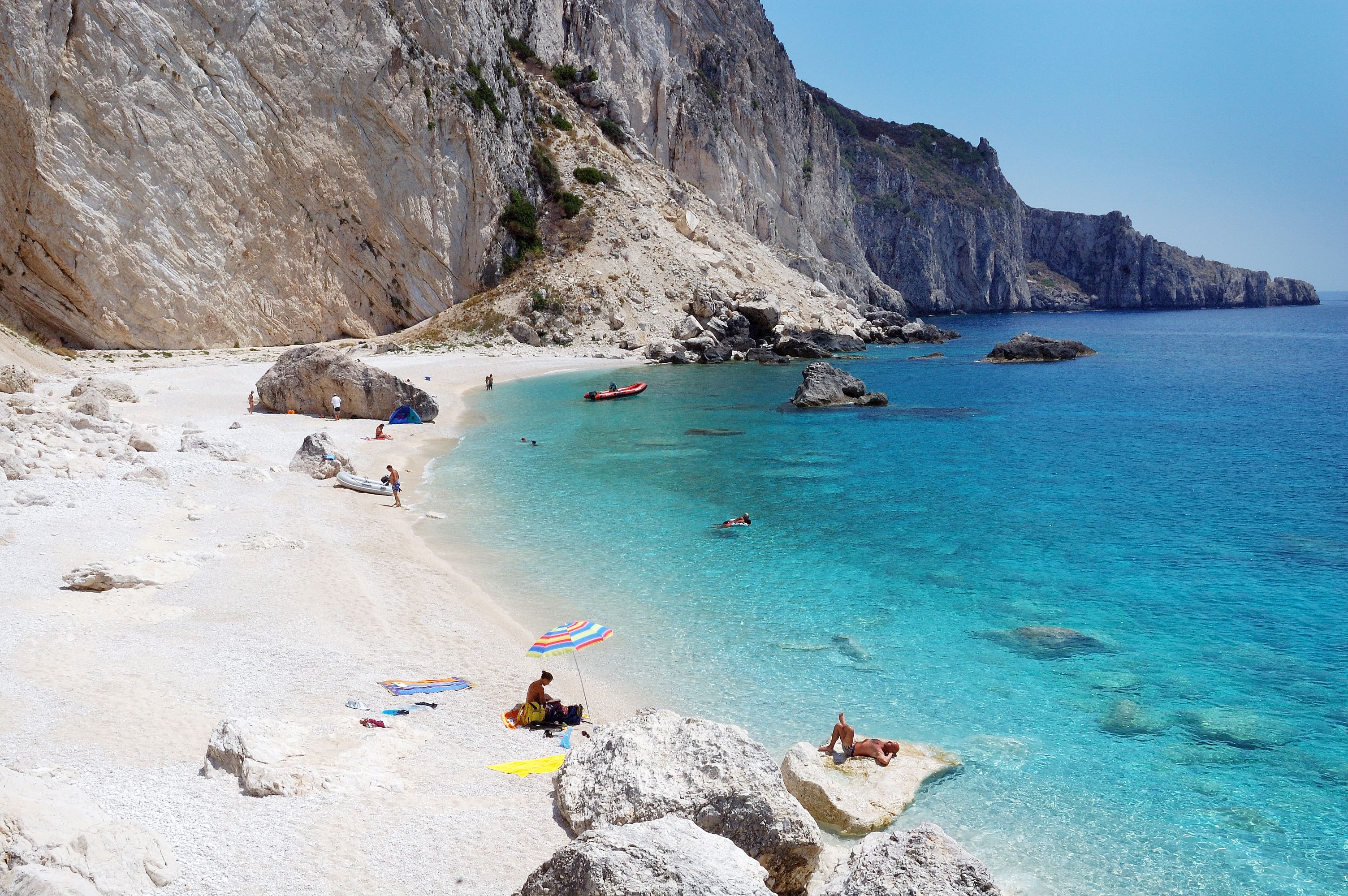 View of a small paradisiacal beach with white sands, towering white cliffs and shallow, crystal-clear water.