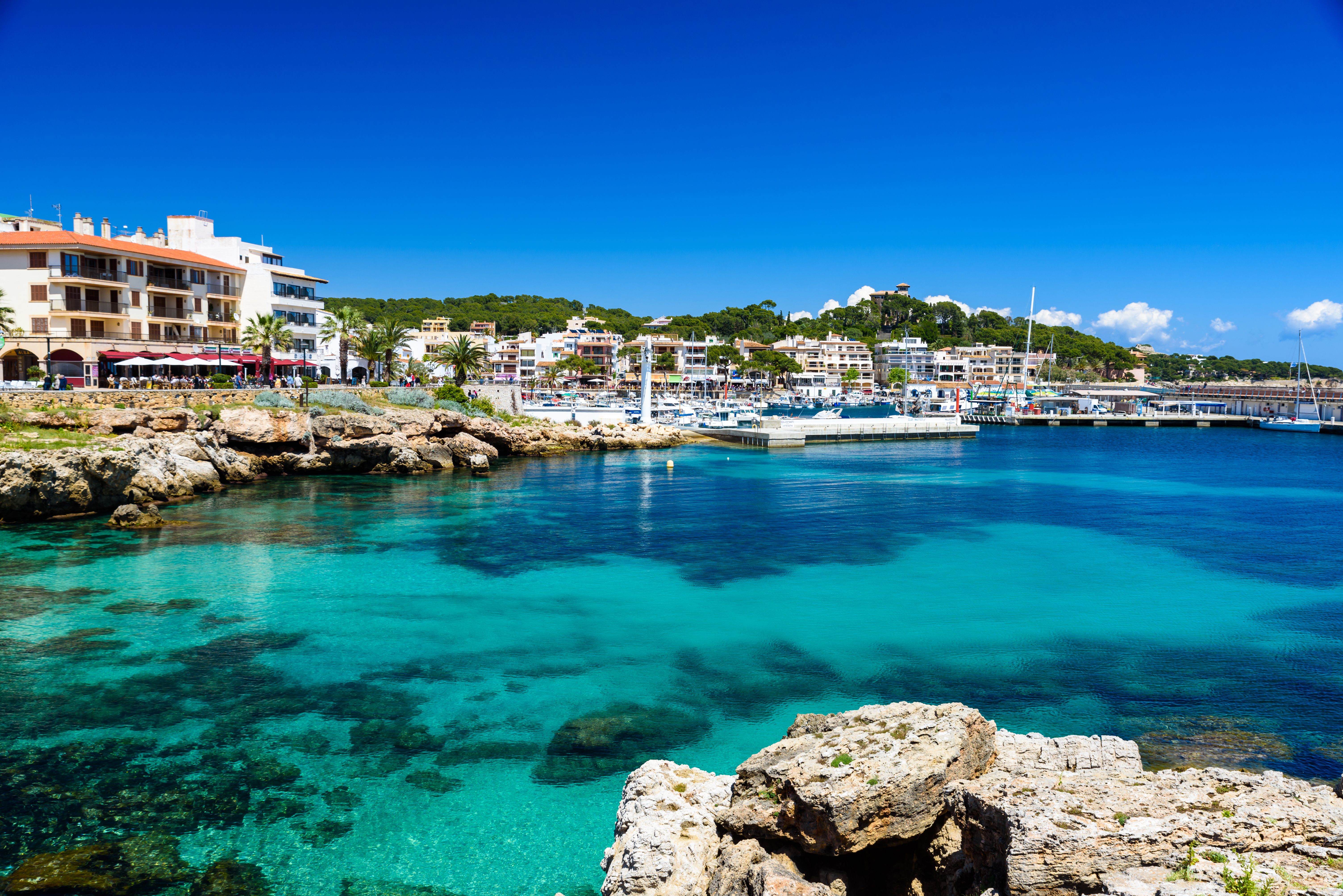 View across the water of Cala Ratjada's harbour and seafront promenade in Majorca