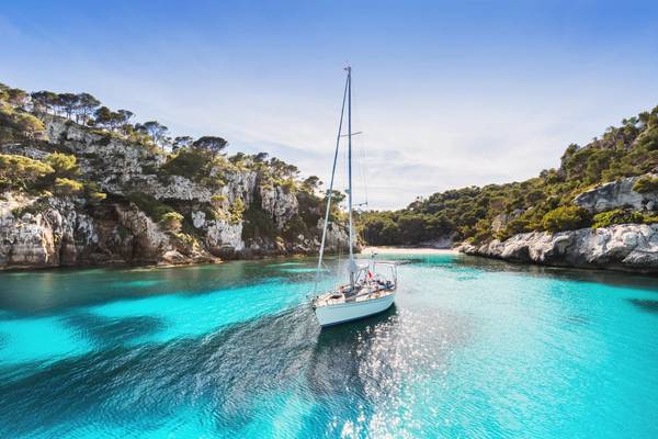 A view of a sailing yacht in a secluded turquoise bay in Menorca, Balearic Islands with a small beach in the background