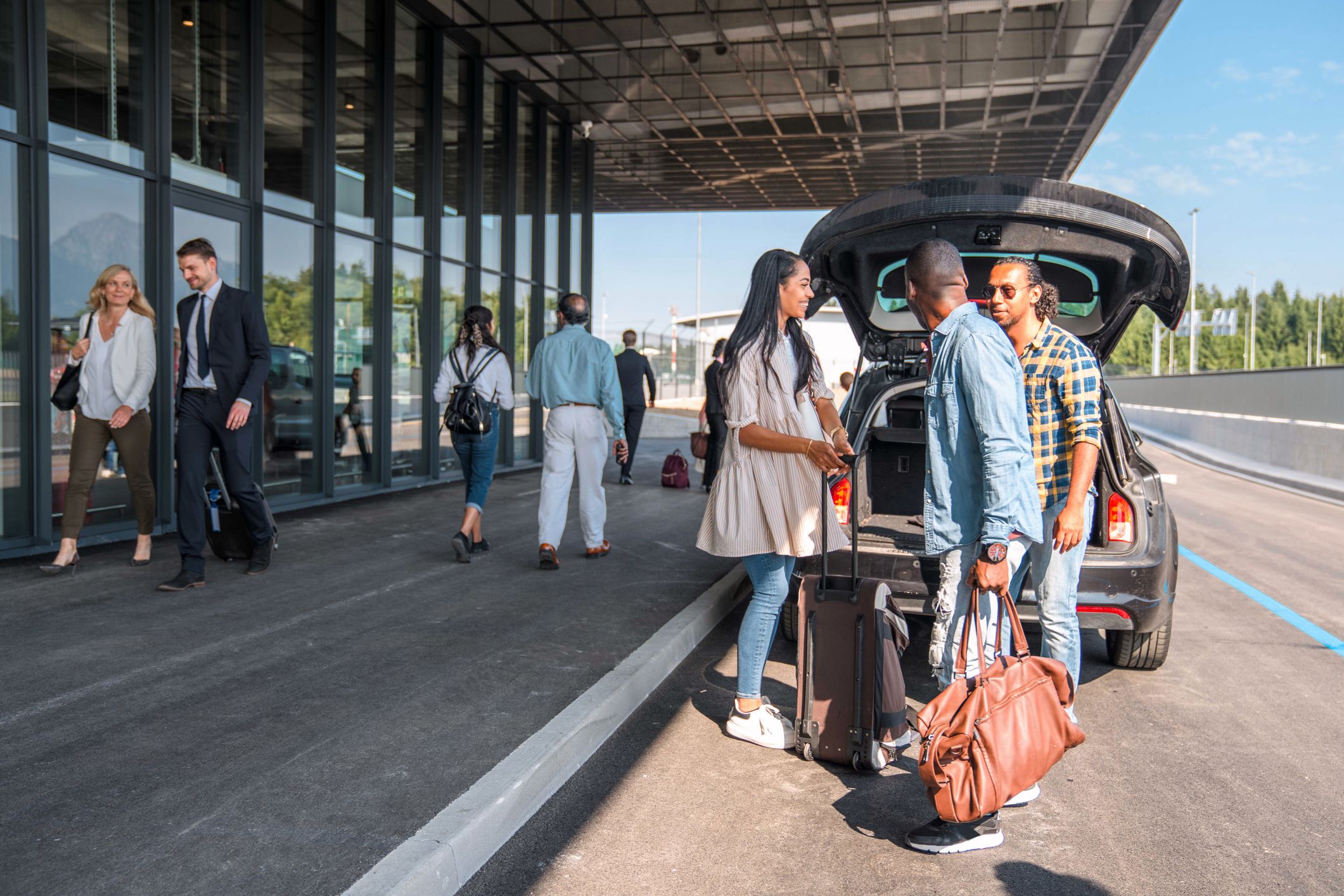 Group of friends unloading luggage from a car and saying goodbyes outside in an airport drop off area
