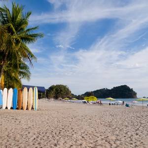An empty beach in Costa Rica with colourful surfboards lined upright on the sand and sun loungers facing the sea
