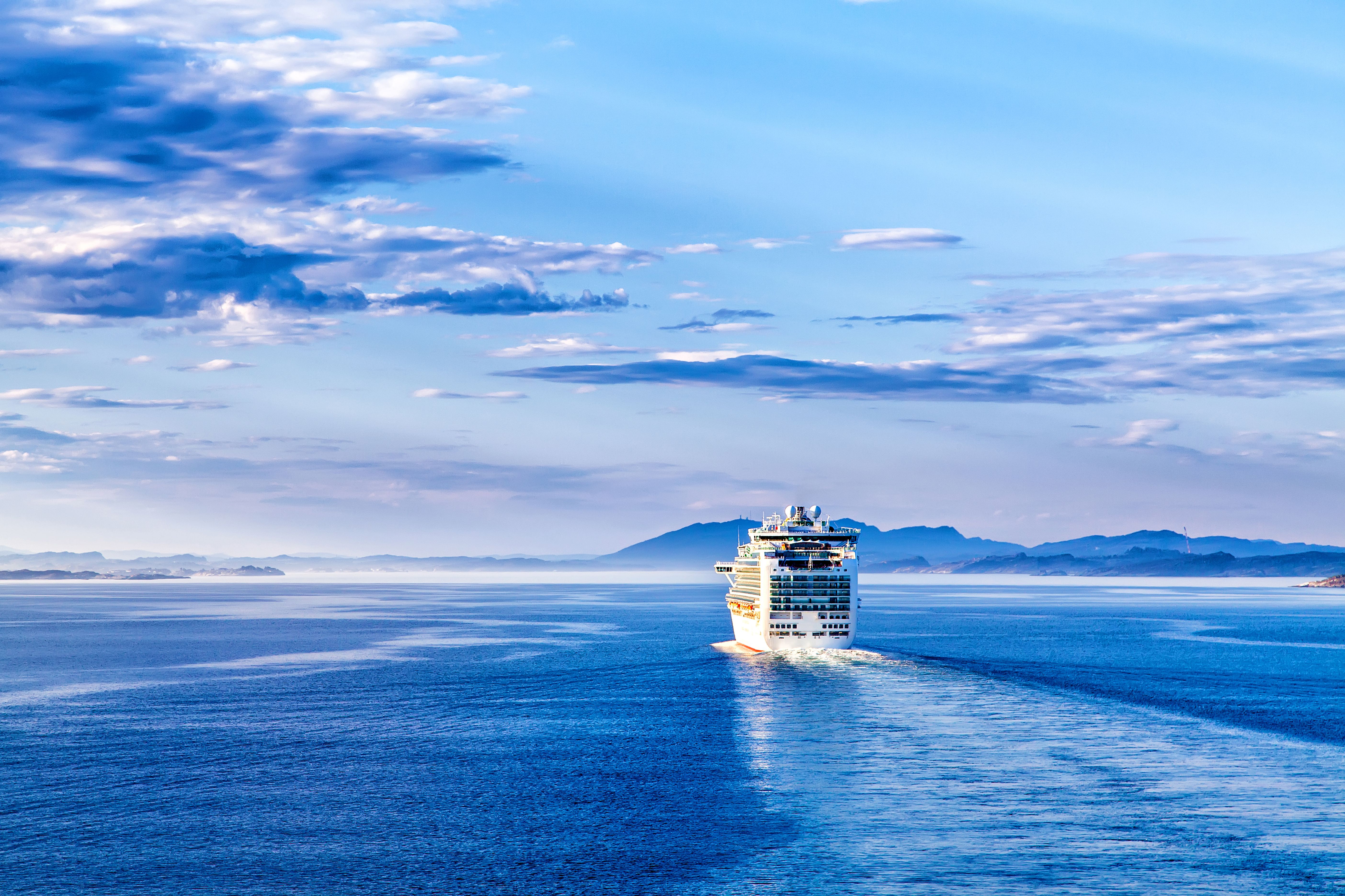 A white cruise liner sailing towards shore on a partly cloudy day